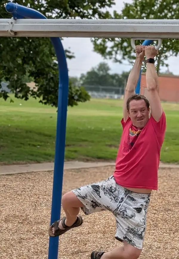 Buford hanging from the rings at a playground, one knee up, grinning